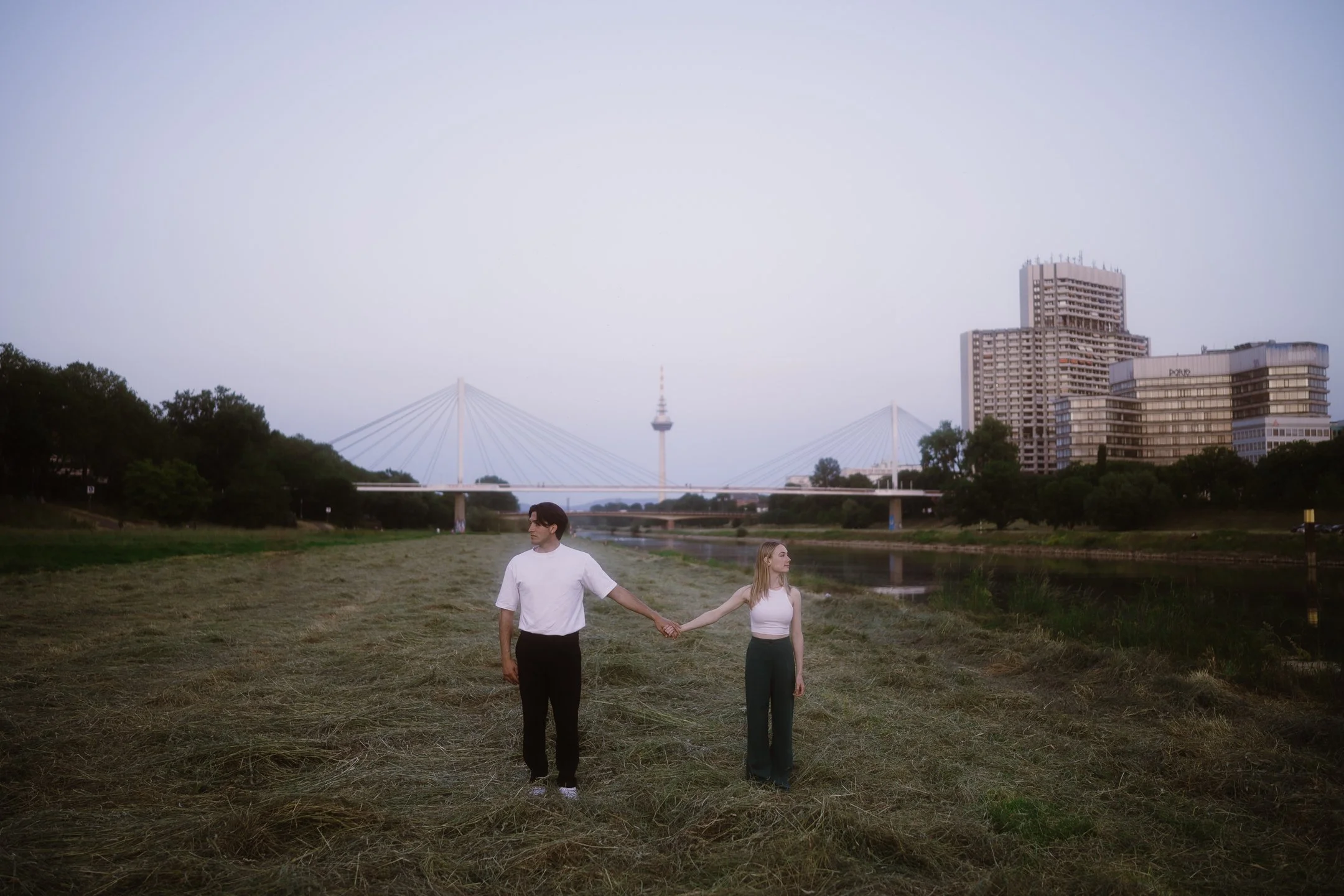 Junges Paar hält Hände vor Fluss und Brücke