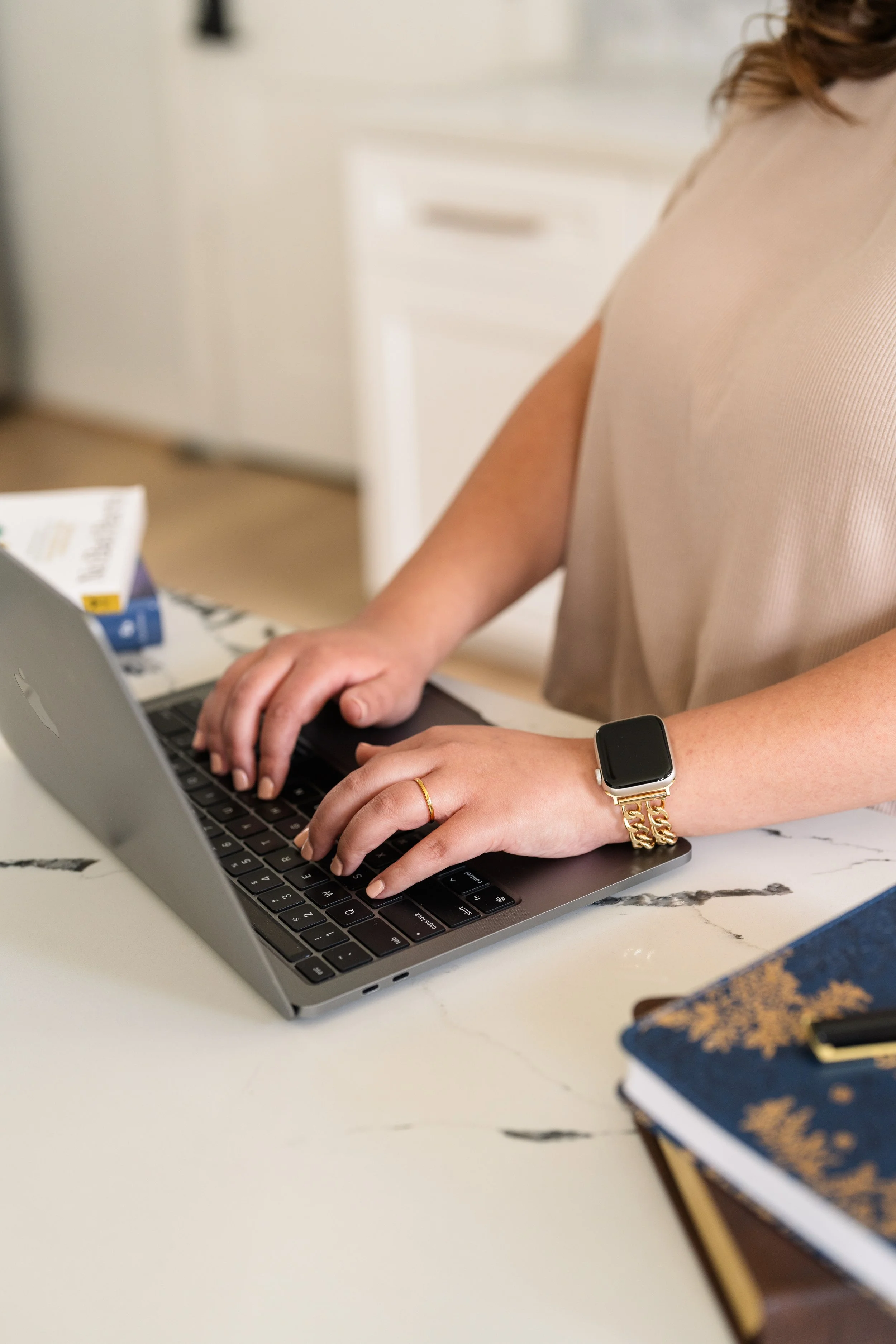 Person wearing a smartwatch and a ring typing on a MacBook laptop in a kitchen