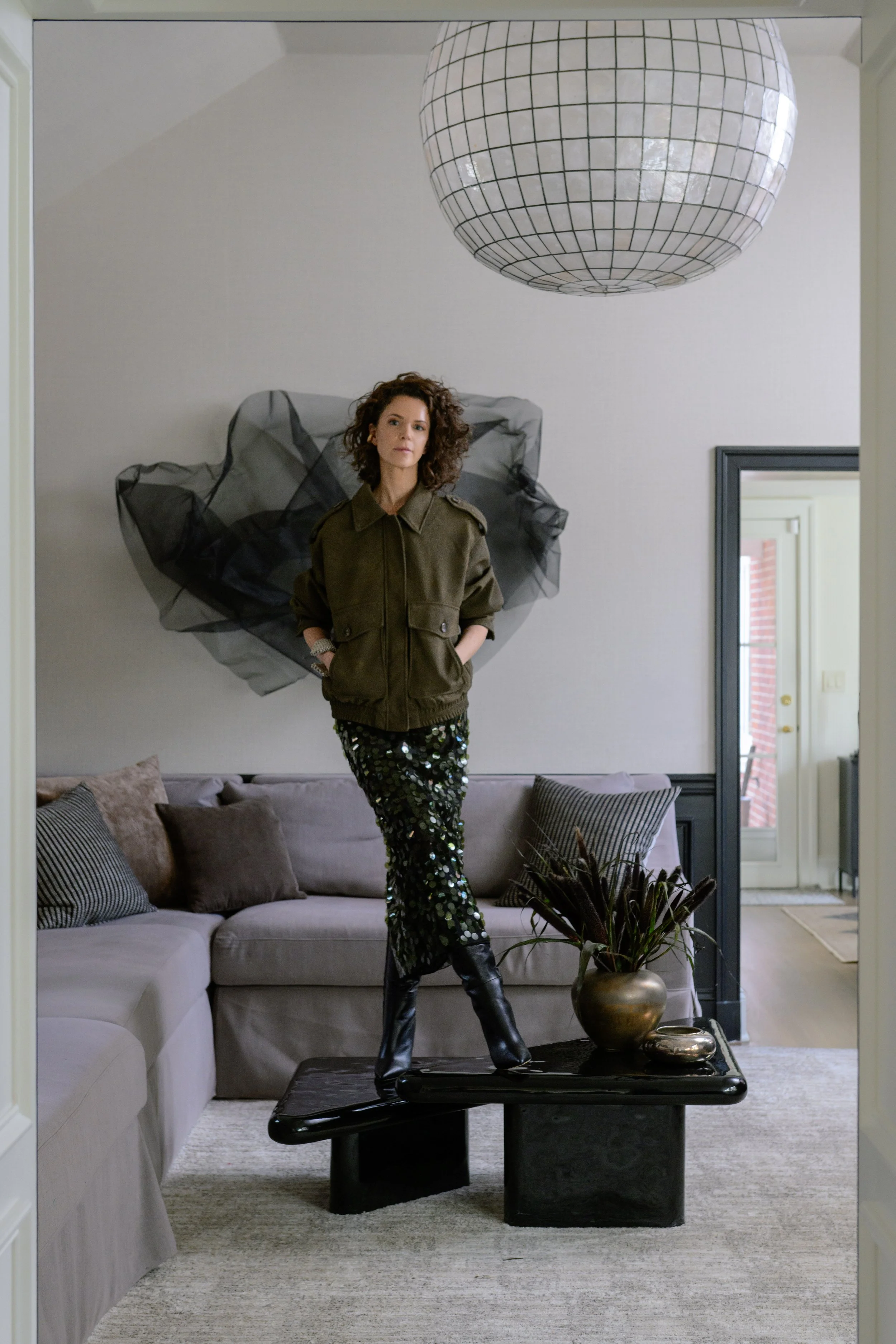  A full-body portrait of Autumn walking through a hallway of her home, with elegant molding and layered furnishings. 