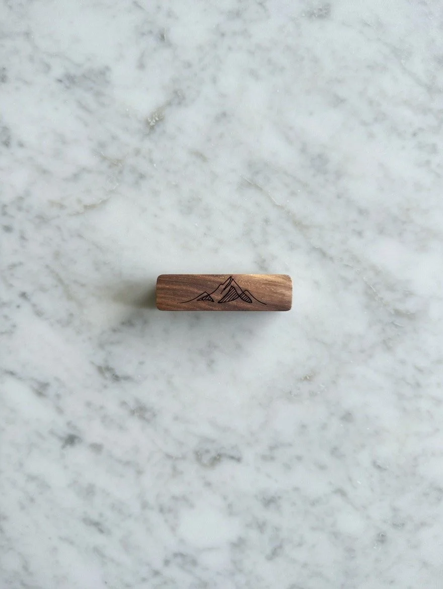 A small wooden stamp with a mountain range design on top, placed on a white marble surface.