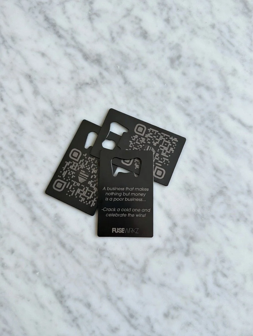 Three black business cards with QR codes and a motivational quote on a white marble surface. Custom logo engraving. Unique business cards