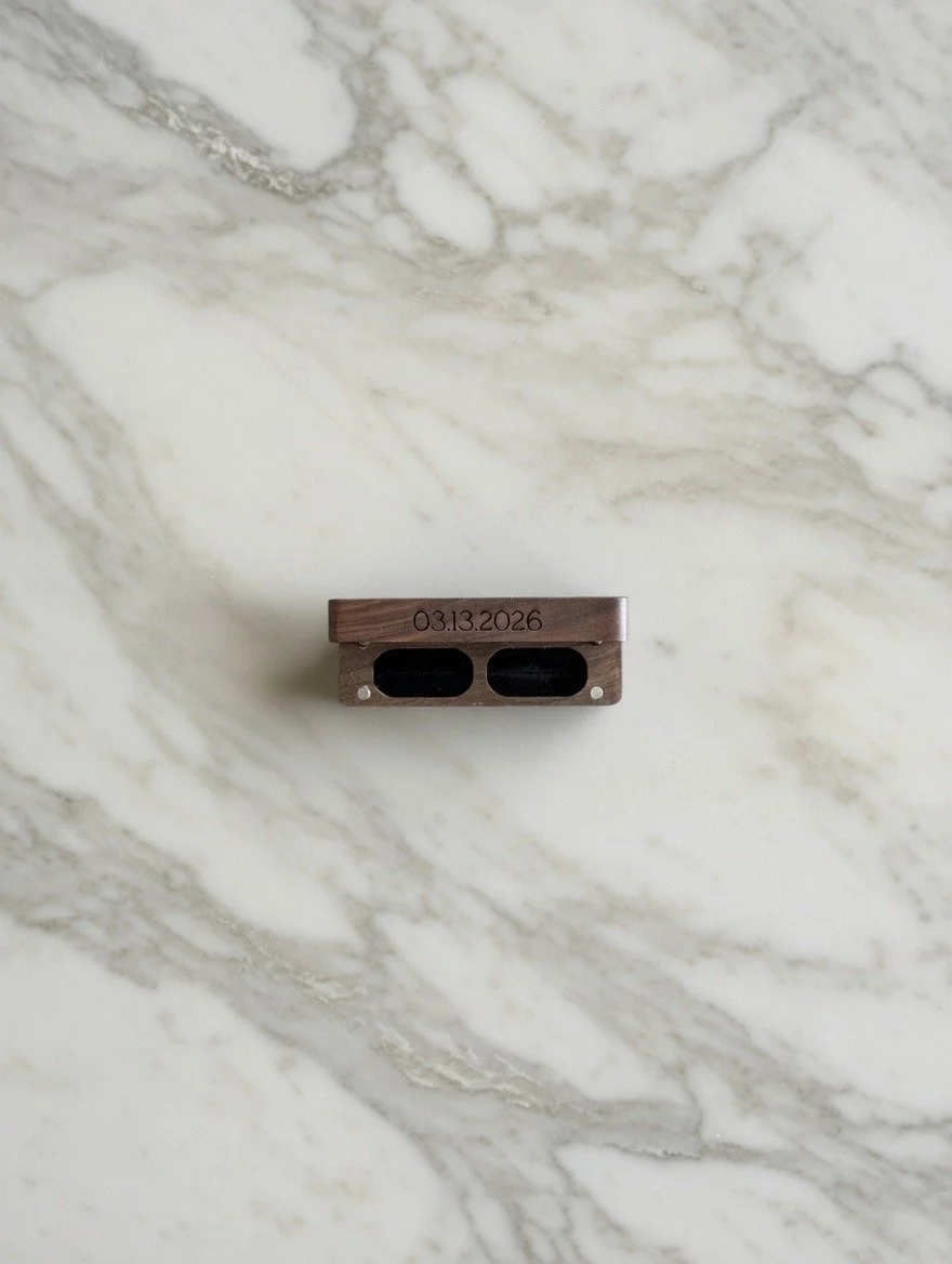Close-up view of a small metallic object with the date "03.13.2026" engraved on it, placed on a white marble surface with gray veins.
