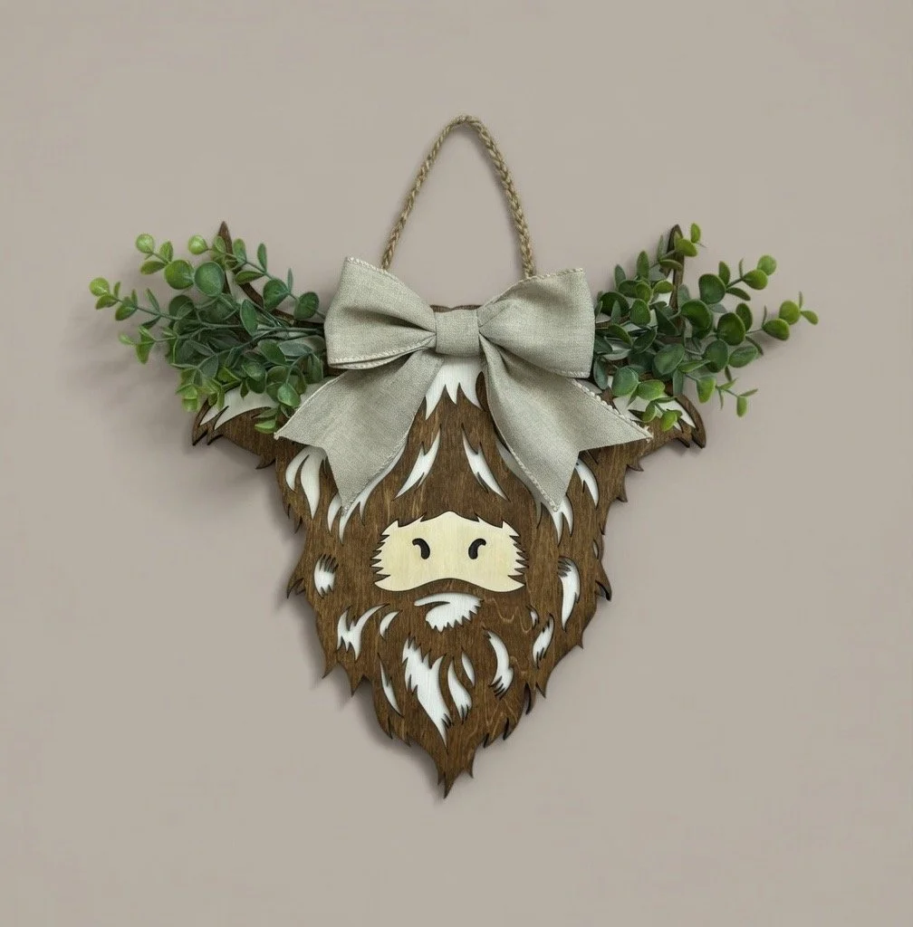 Wooden wall hanging of a cartoonish Yoda face with a beard, decorated with green foliage, a gray bow, and a jute hanging loop.
