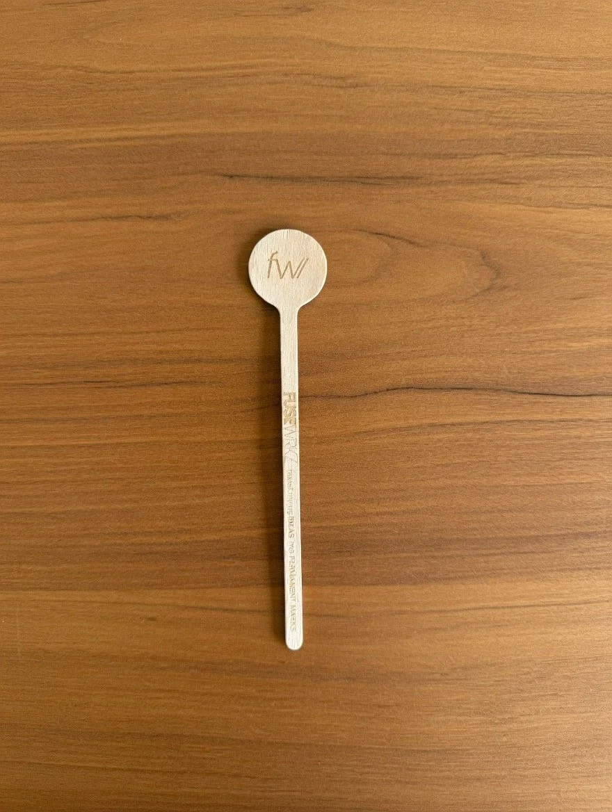 A wooden tongue depressor with a circular end and engraved text on the handle, placed on a wooden surface.