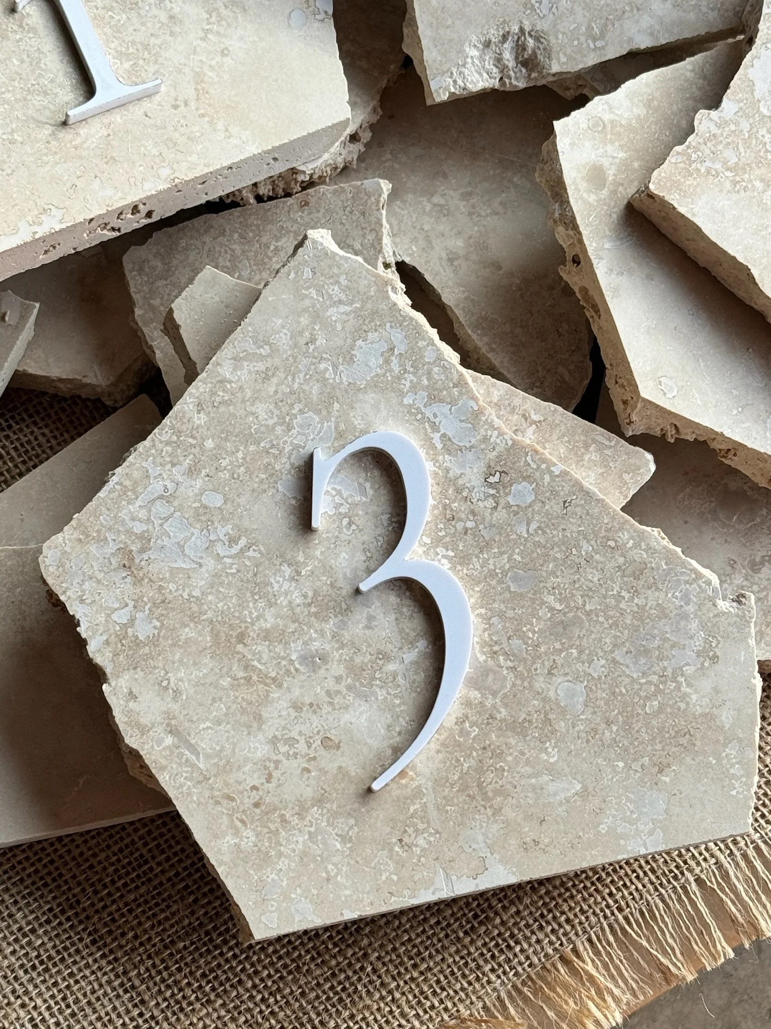 A stack of custom, stone table numbers, placed on a woven mat. Great for wedding table numbers