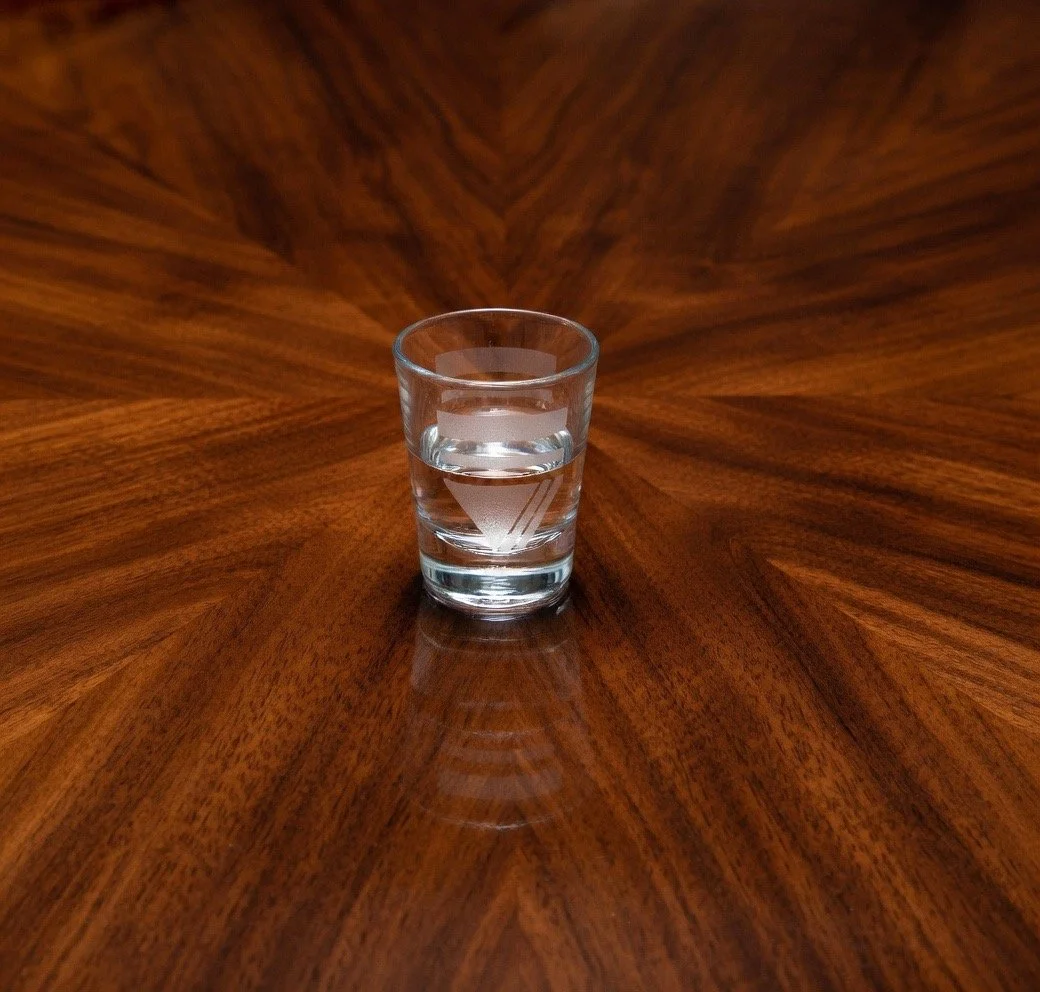 A glass of water on a polished wooden surface with a distinctive starburst grain pattern.