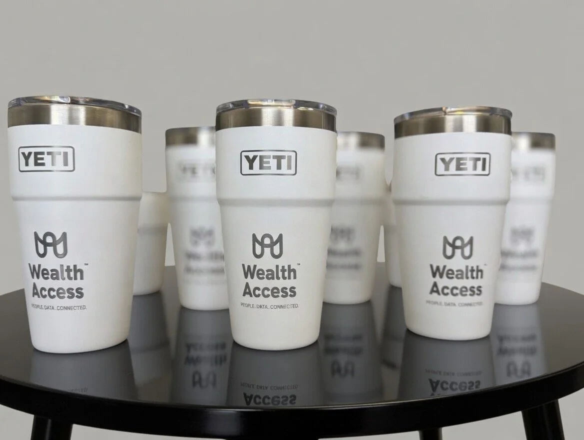 Multiple white YETI tumblers with 'Wealth Access' logo and stylized glasses icon, arranged on a black table.