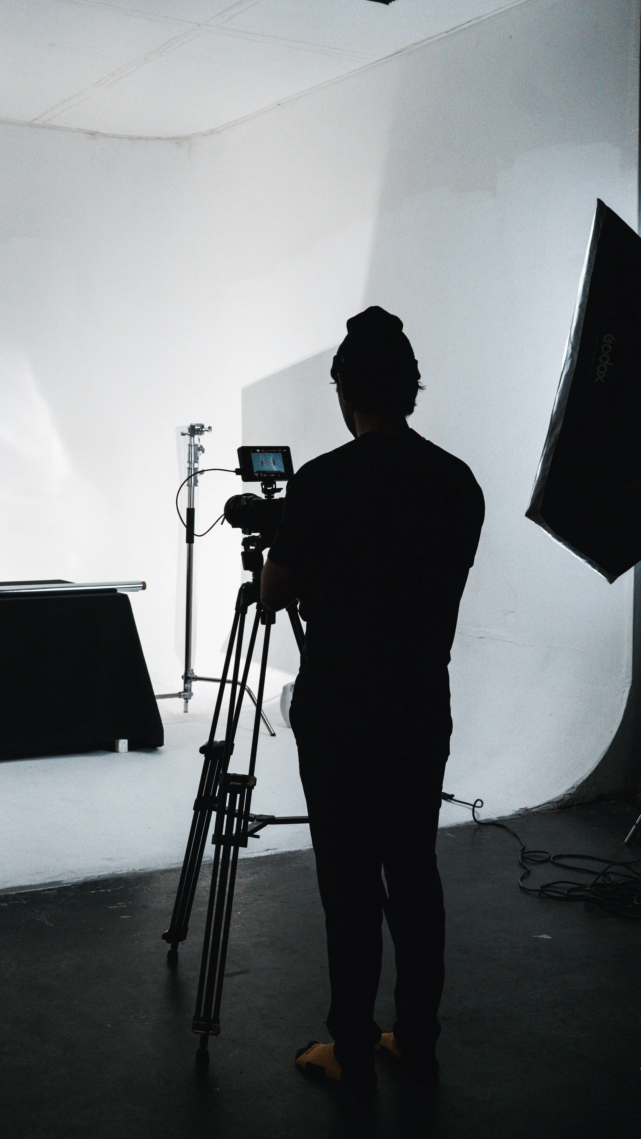 Silhouette of a person filming in a photo studio with professional lighting equipment and a white background.
