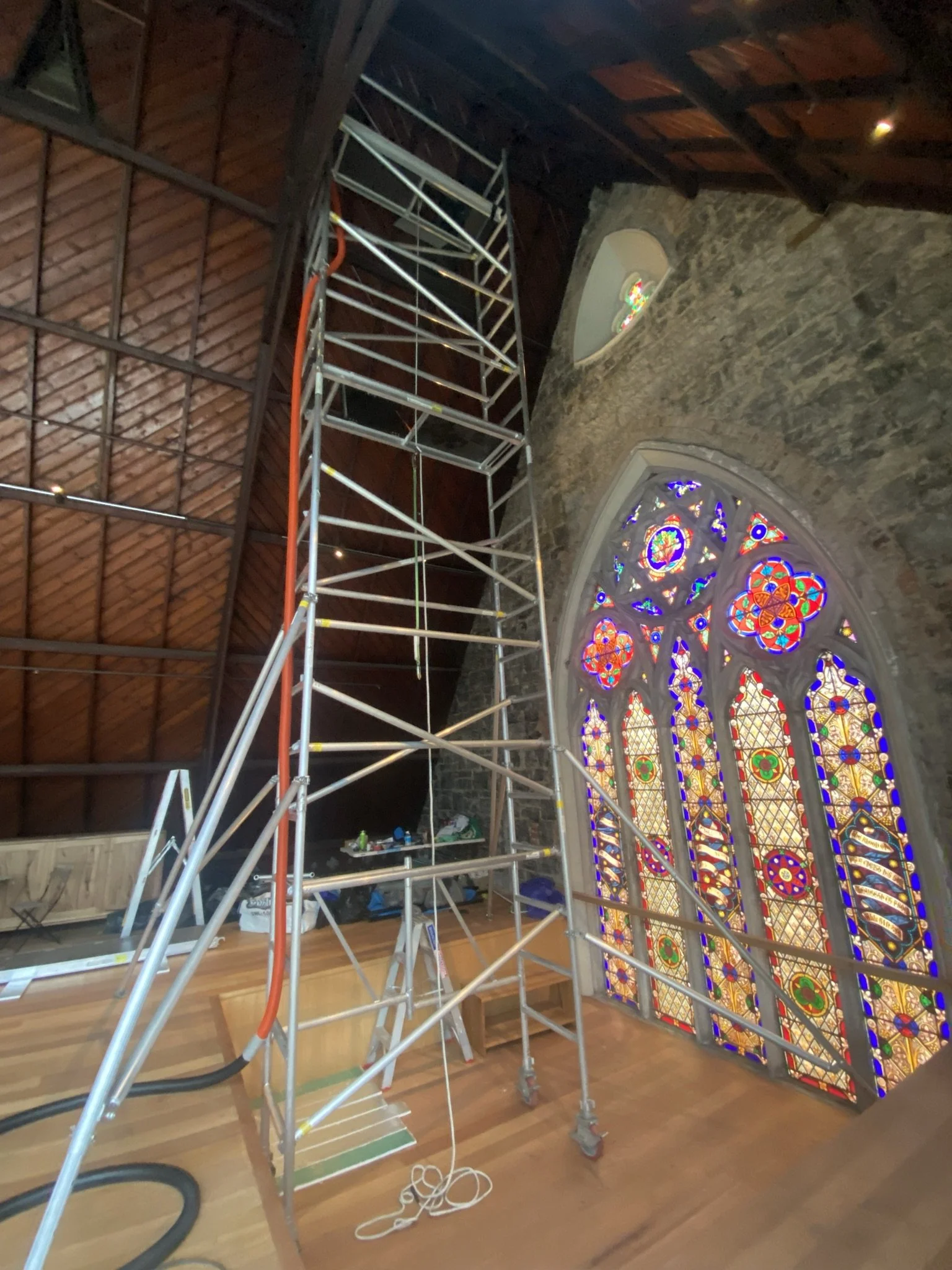 Interior of a church or cathedral under renovation with scaffolding in front of a large, colorful stained glass window.