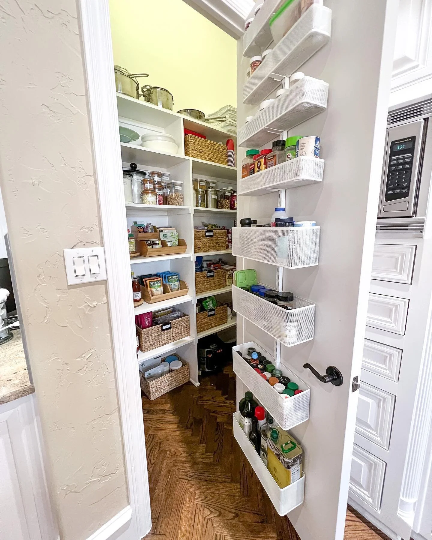 Pantry with shelves filled with jars, spices, and canned goods, with white storage bins on a door organizer.