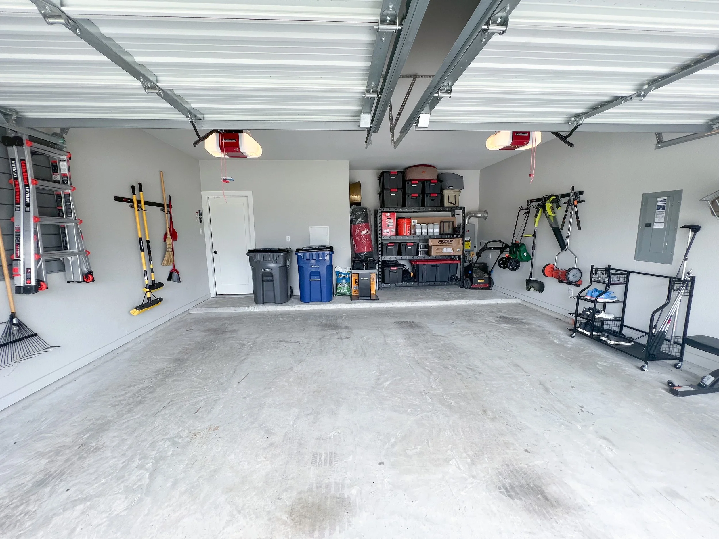 Empty garage with organized shelves, storage bins, and cleaning tools on the walls.