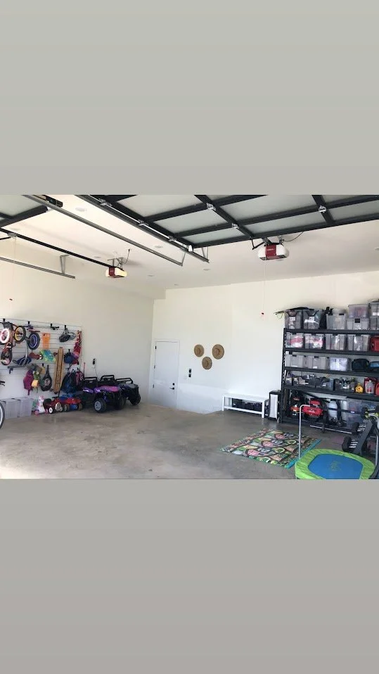 Empty garage with a few children's ride-on toy vehicles, organized storage shelves, and garage tools.
