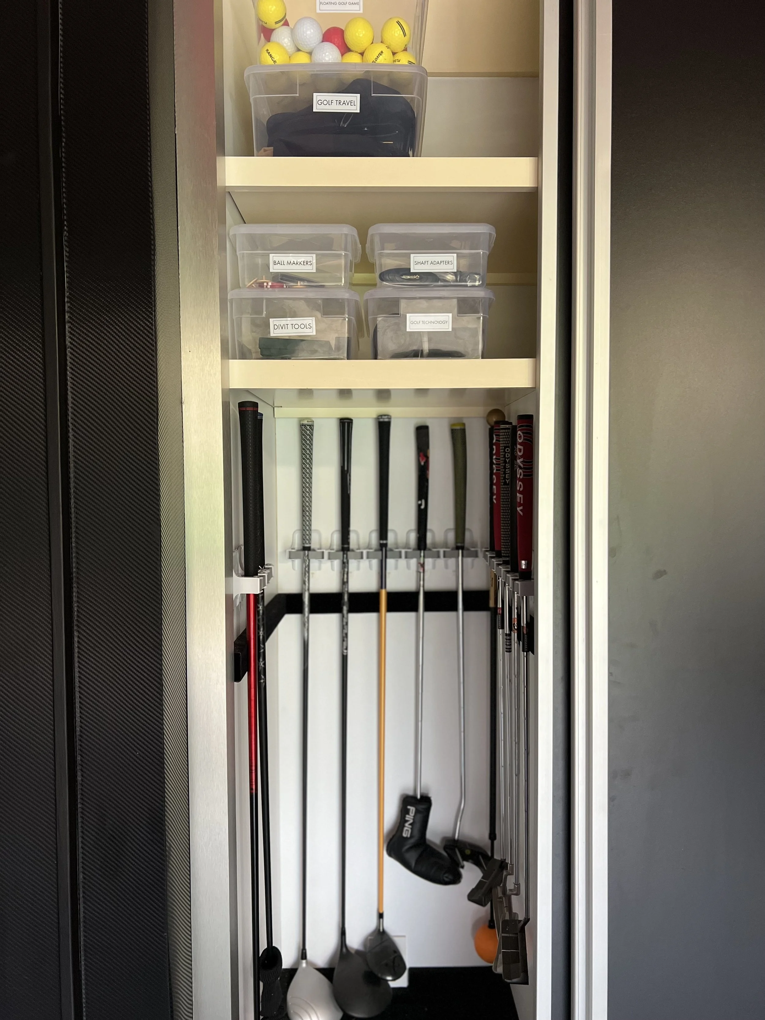 A golf equipment storage closet with labeled plastic drawers containing golf-related items and a closet rod holding golf clubs.
