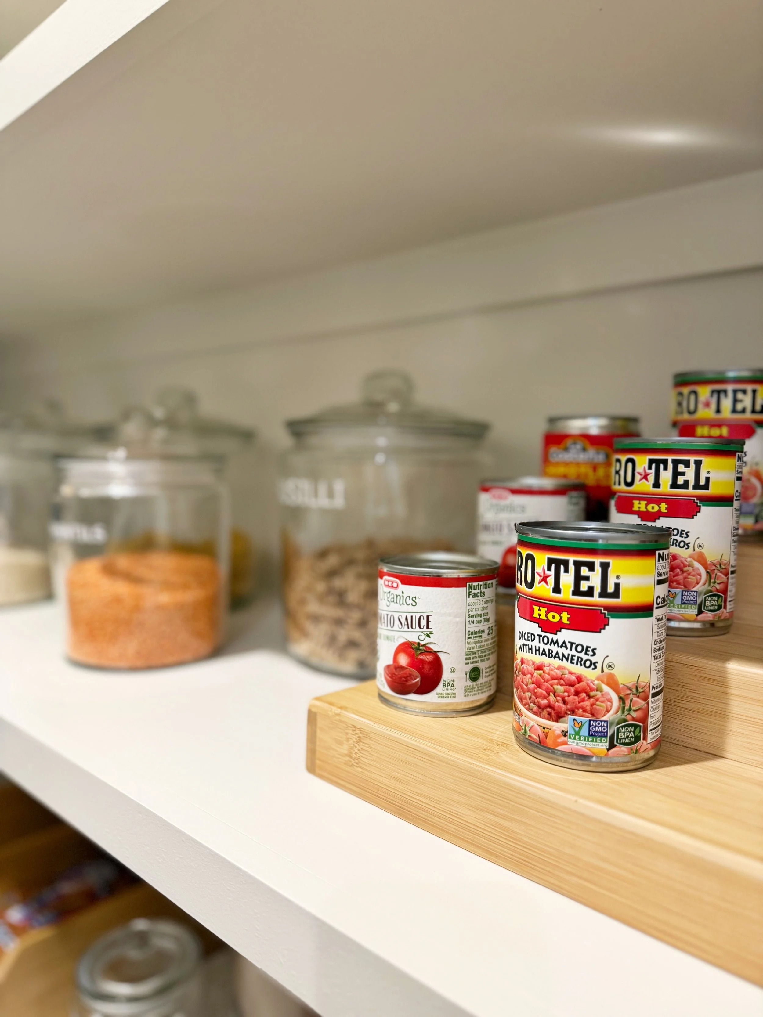 Canned diced tomatoes with habaneros, tomato sauce, and other jars on a kitchen shelf.