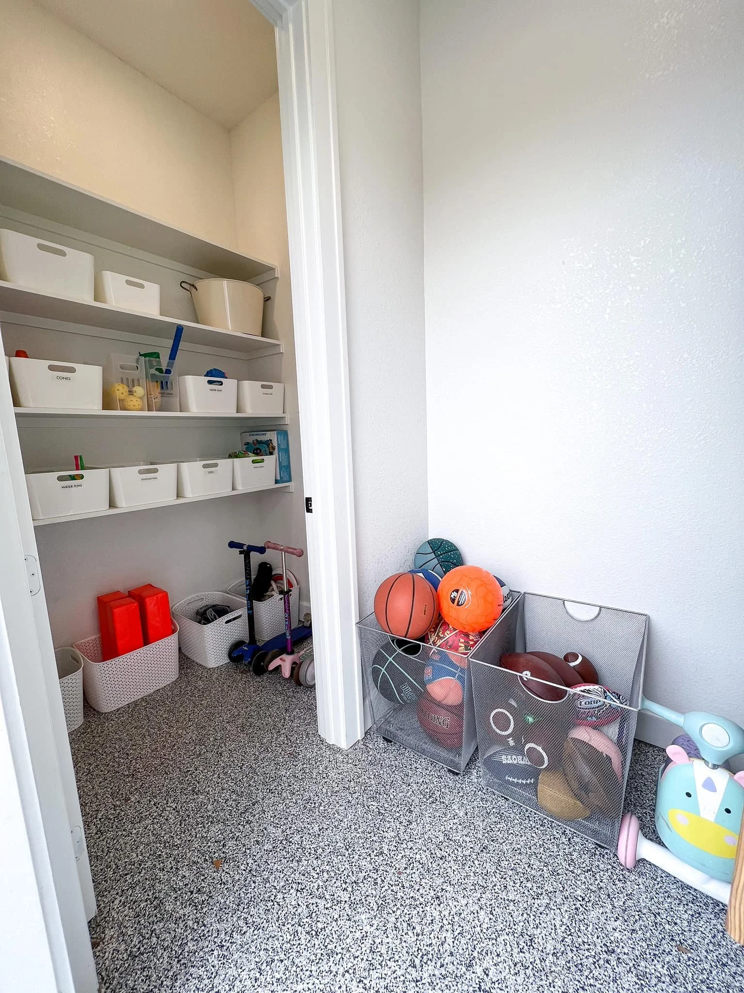 A playroom with toys, sports balls, scooters, and storage bins, with a closet containing additional toys and supplies.