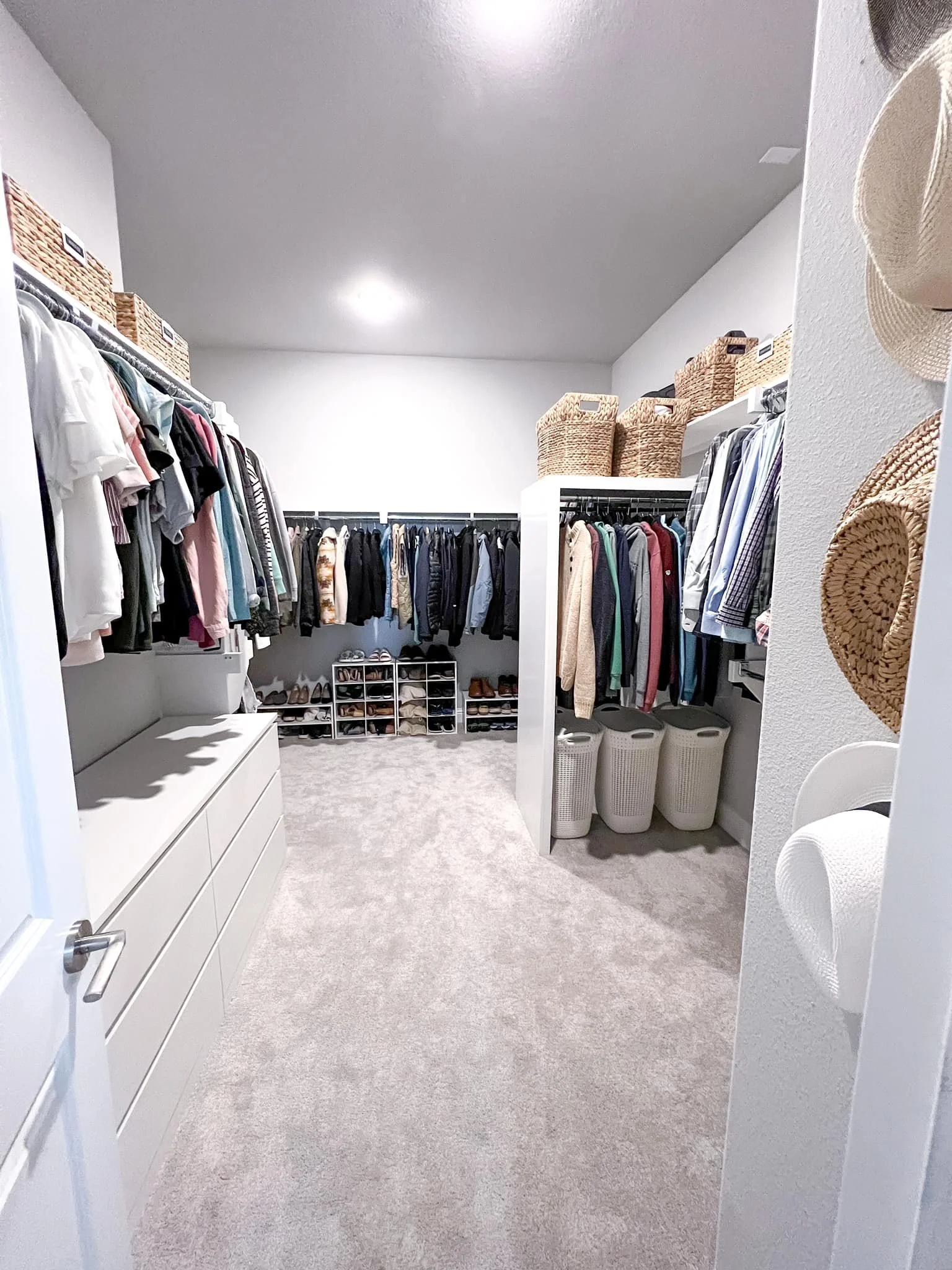 A spacious walk-in closet with hanging clothes, storage baskets, shelves with shoes, and laundry baskets.