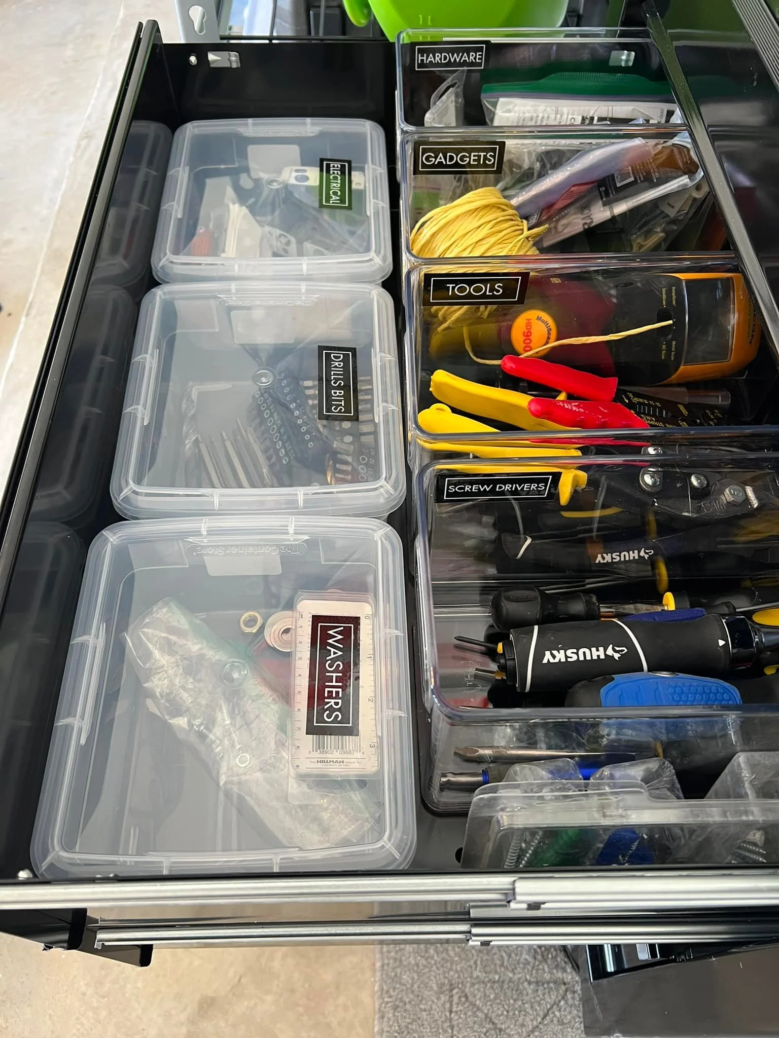 Organization of tools and hardware in transparent plastic bins, labeled for electrical, drills bits, washers, hardware, gadgets, tools, and screw drivers, on a workbench.
