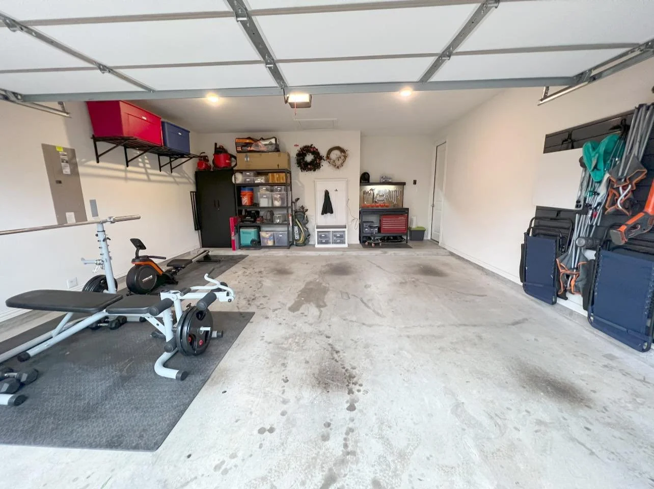 Empty garage with workout equipment, storage shelves, and holiday wreaths on the wall.