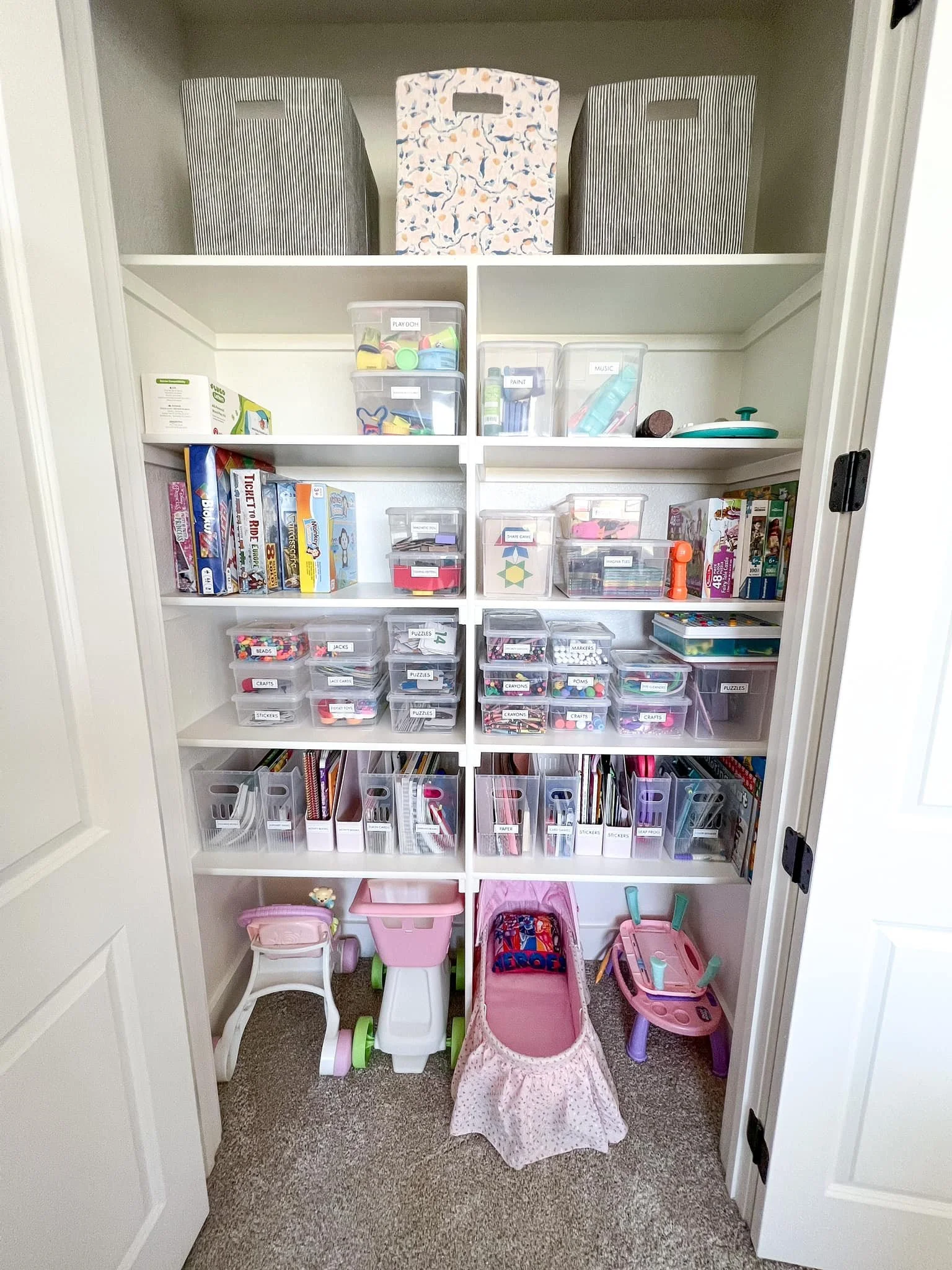 A closet with organized shelves containing toys, books, and storage bins, along with some children's ride-on toys on the carpeted floor.