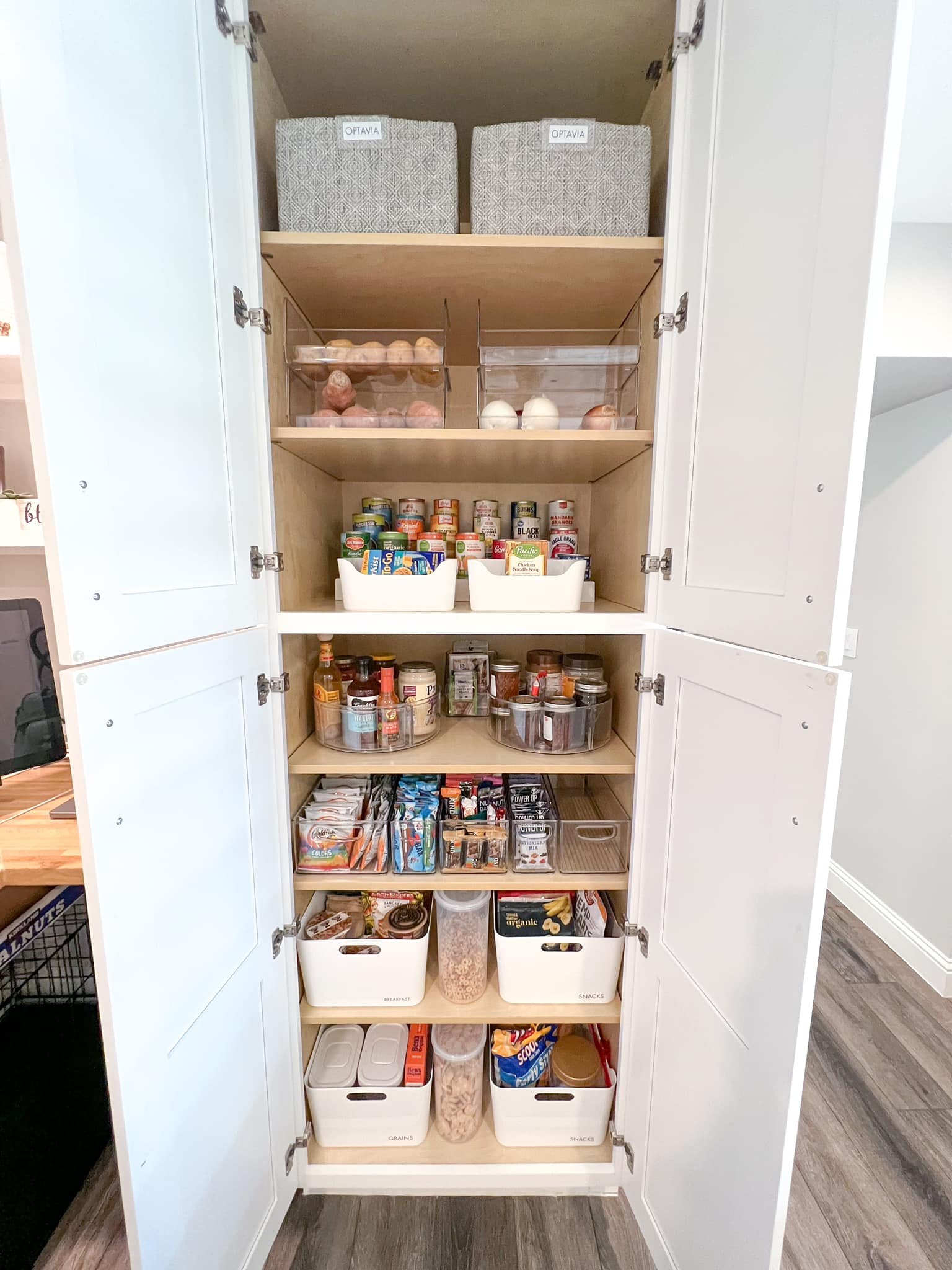 Open pantry cabinet filled with canned goods, snacks, spices, and storage bins.