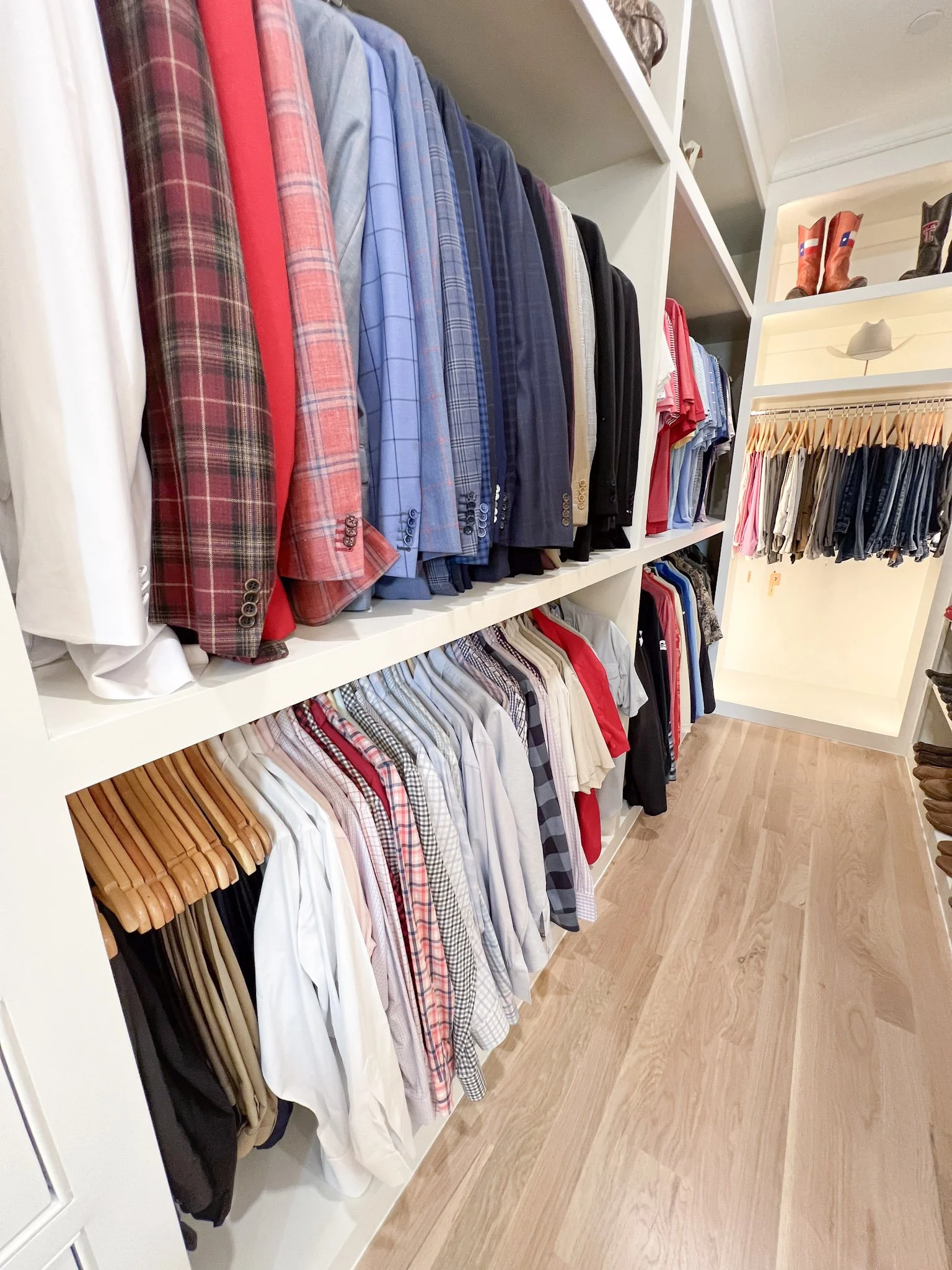 Organized men's clothing closet with suits, shirts, and pants on white shelves.