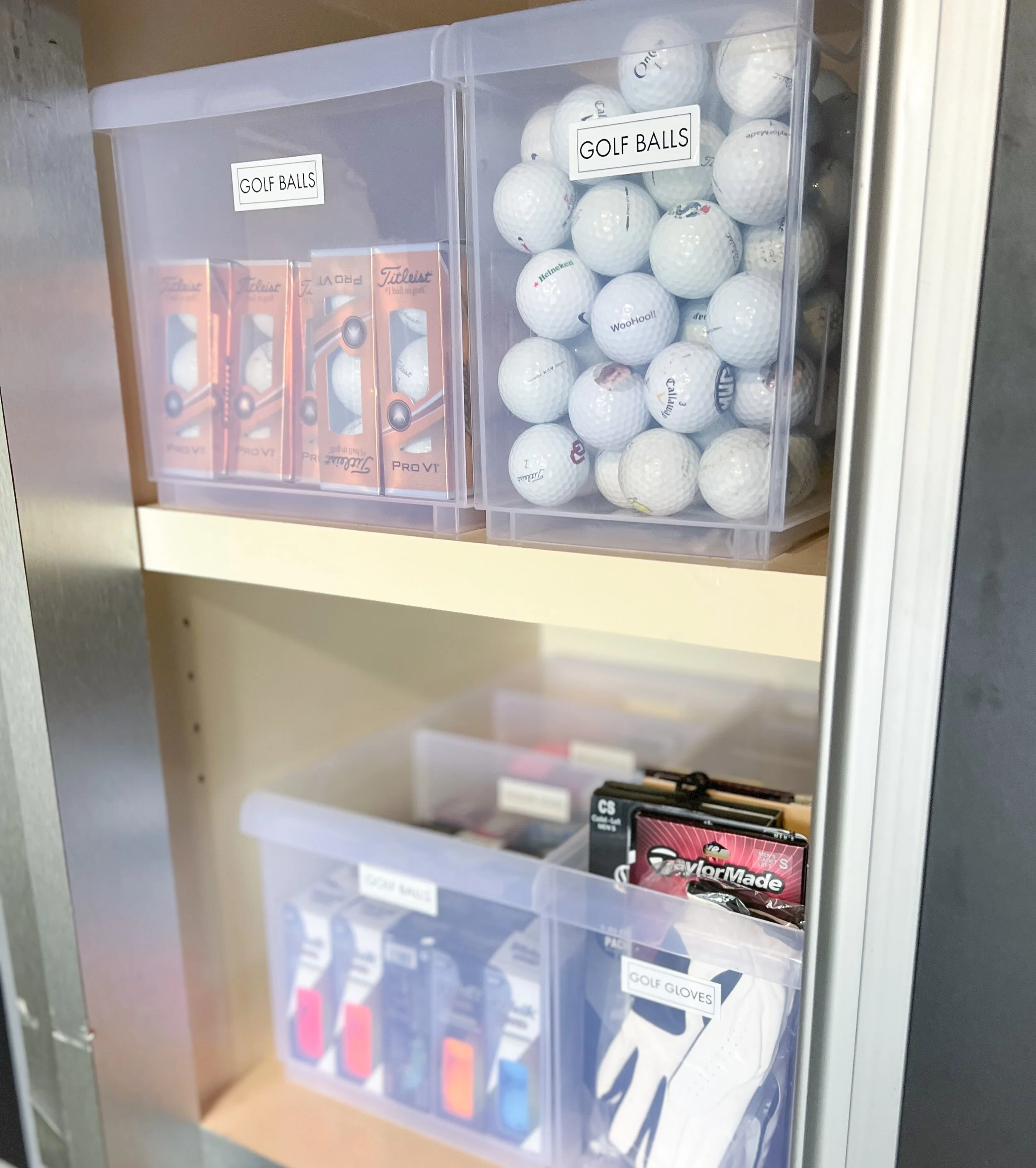 Storage cabinet with golf equipment: top shelf contains boxes of golf balls, middle shelf has more golf balls in a clear container, lower shelf holds golf glove packaging and golf ball markers.