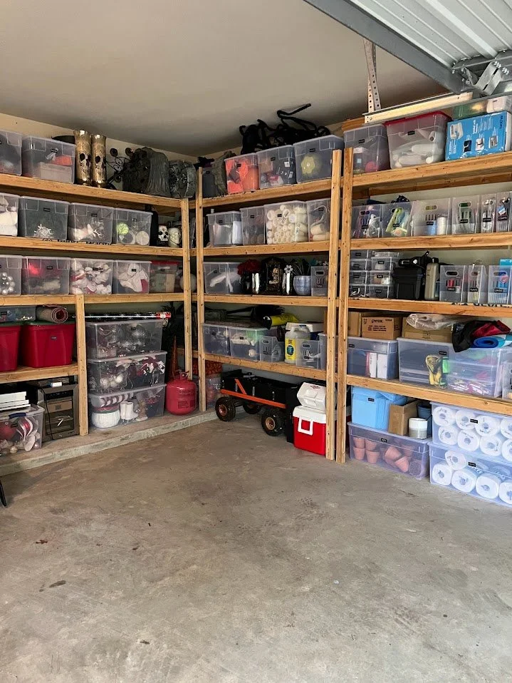 A garage storage area with wooden shelves filled with plastic bins, tools, and supplies, and a concrete floor.