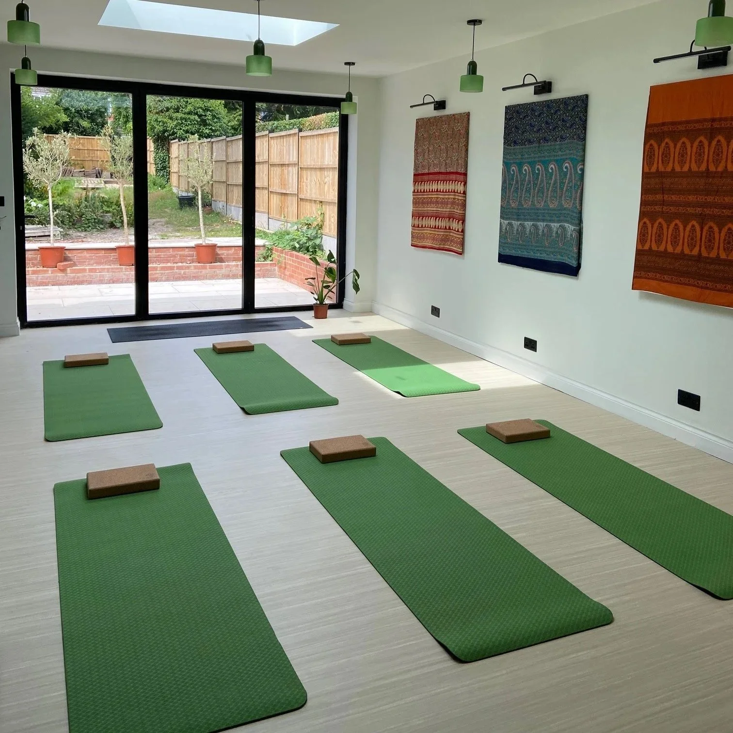 Indoor yoga or meditation space with six green mats and cork blocks, large sliding glass doors leading outside, and woven wall hangings.