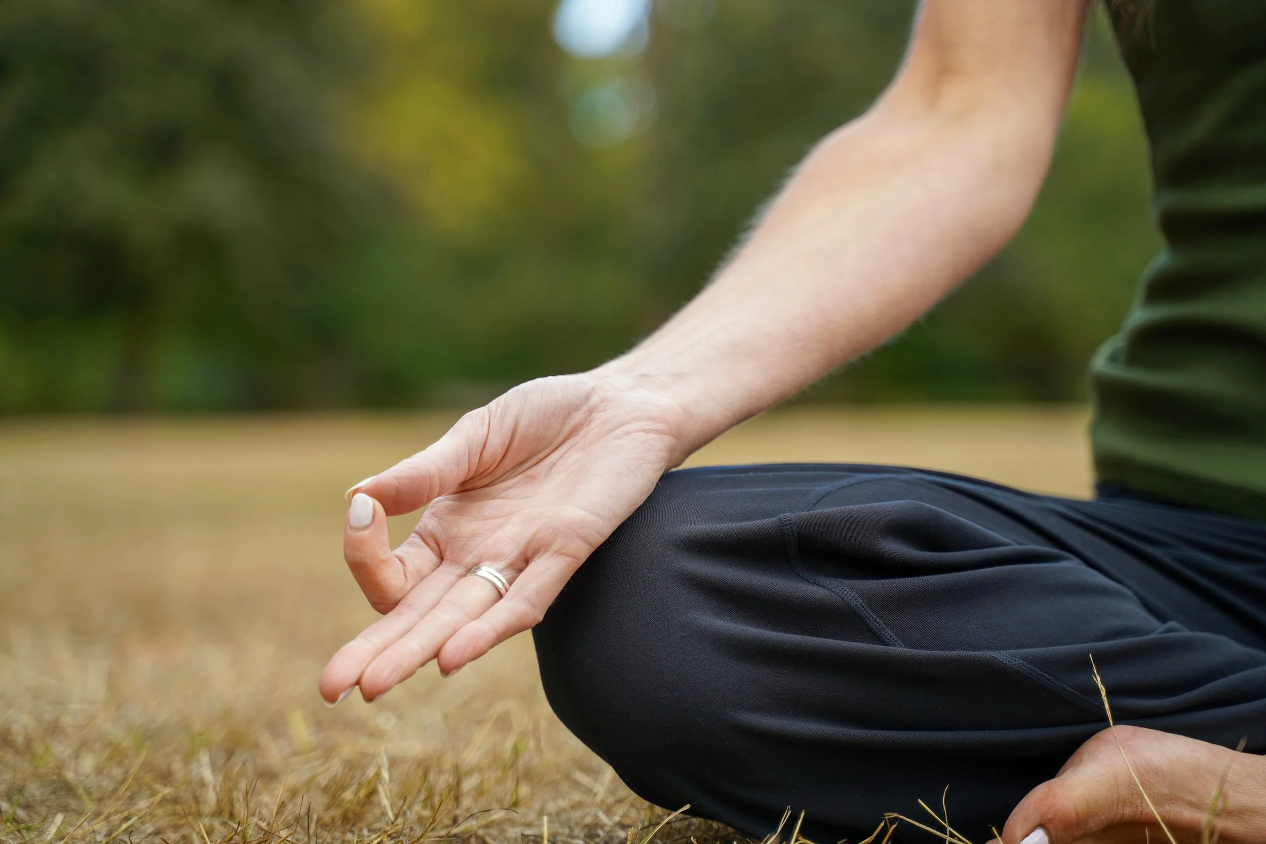 A person practicing yoga outdoors on grass, meditating in lotus position using gyan mudra hand gesture
