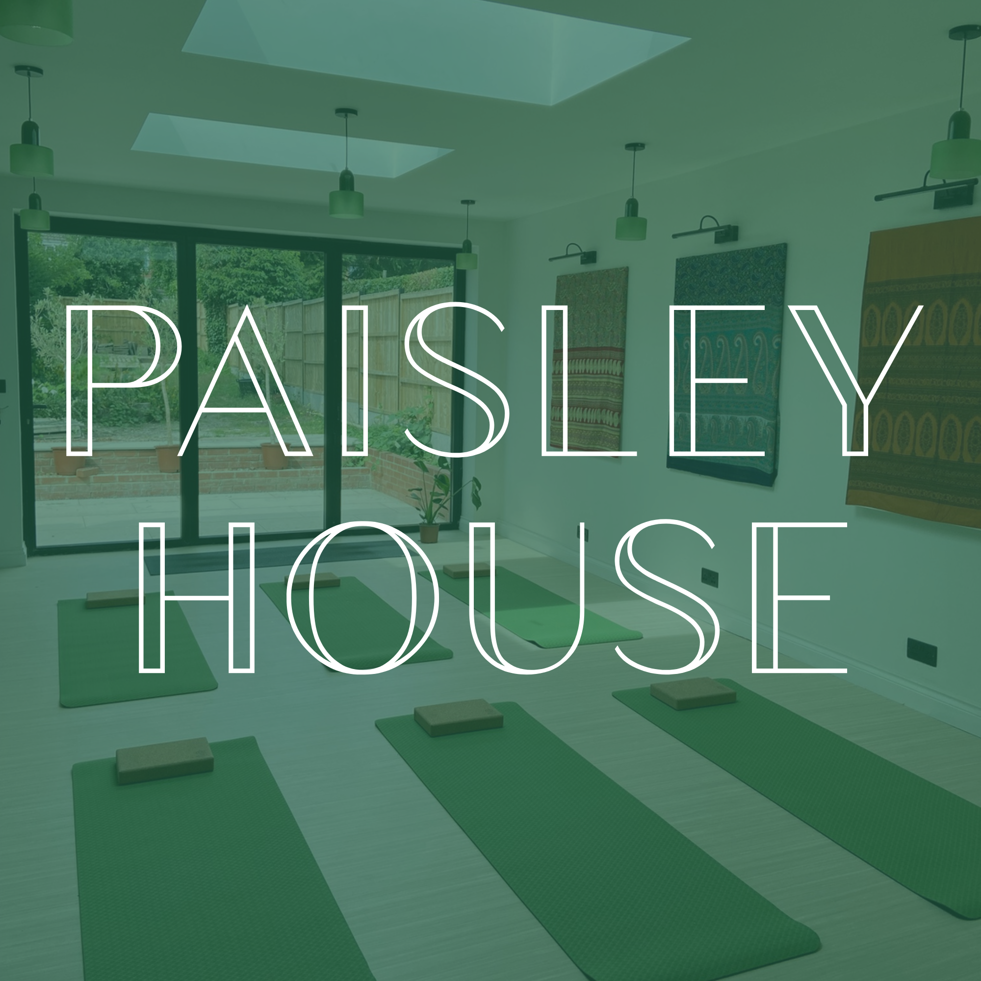 Paisley House yoga studio space in Dorridge, Solihull with green yoga mats and blocks arranged on the floor, large glass sliding doors leading outside, and framed artwork of vintage saris hanging on white walls.