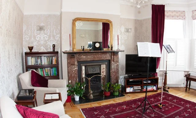 Living room with fireplace, bookshelves, flat-screen TV, and music stand, decorated with red curtains and rug.