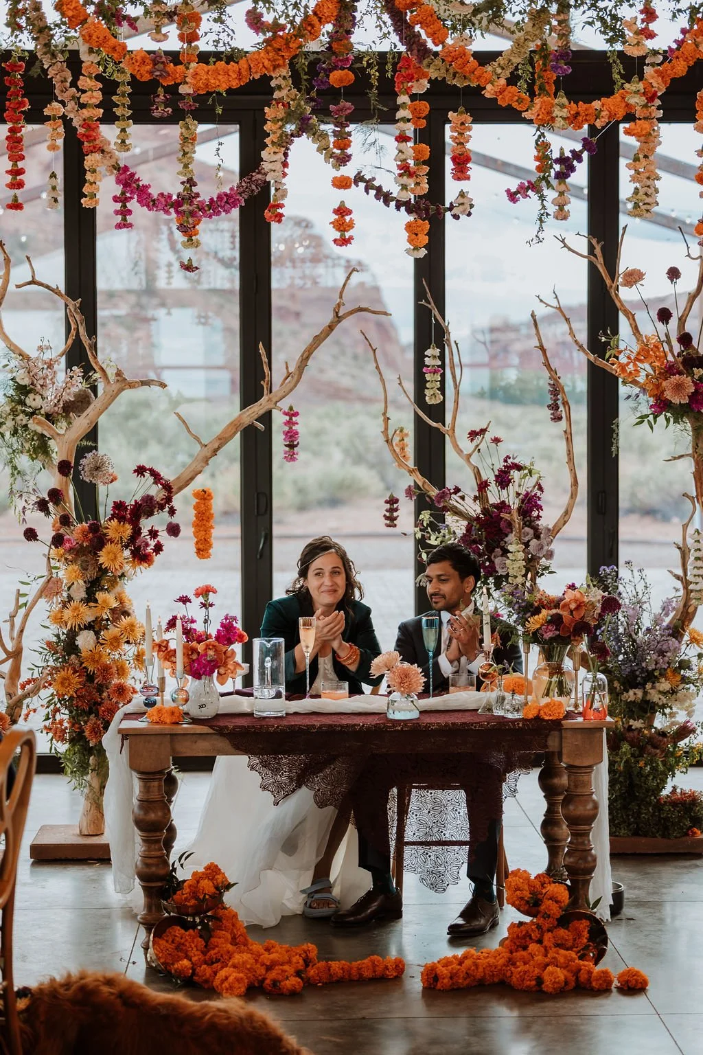 indian wedding in Moab at the Red Earth Venue couple sits at sweeteart table surrounded by flowers