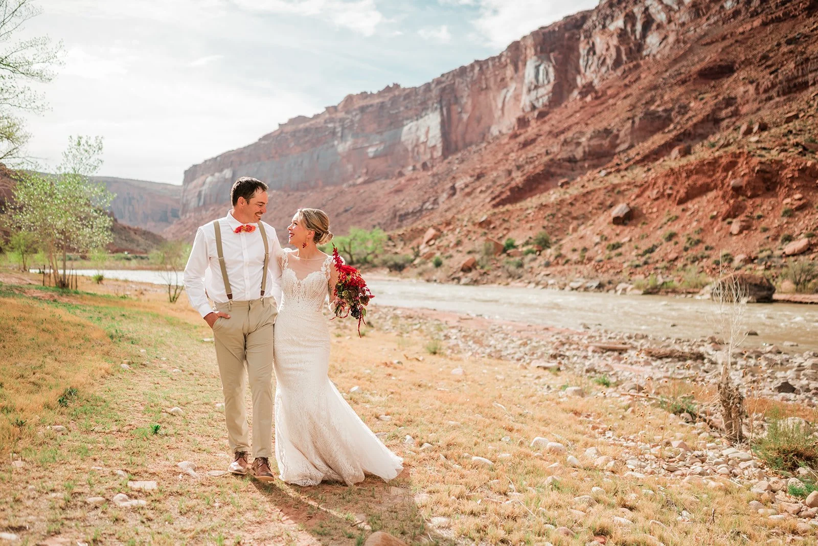 Couple walking on the desert floor along the Colorado River at Red Cliffs Lodge with the red rock bluffs in the background