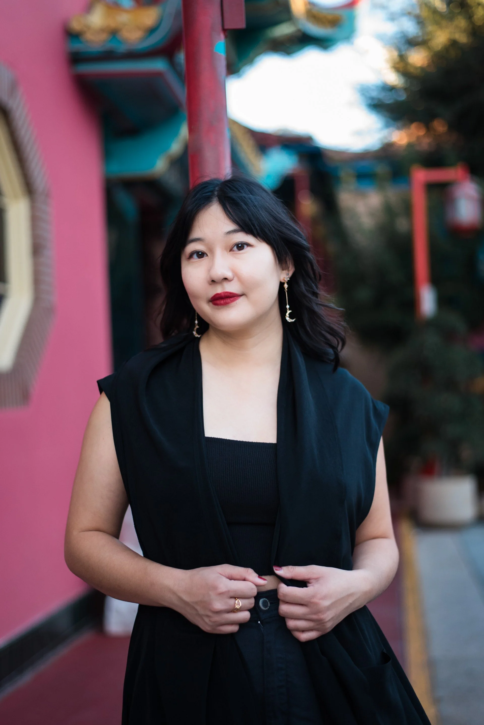 Photo of Lilly smiling at the camera, standing in front of a white wall with greenery