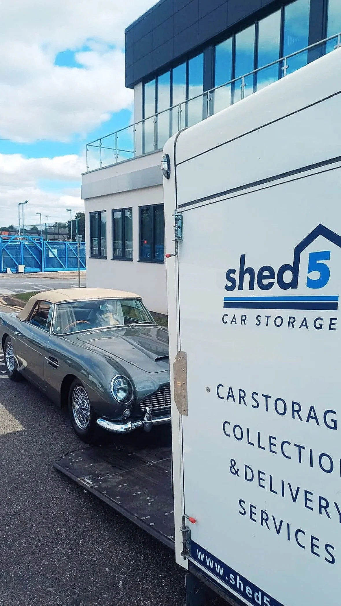 a vintage Aston Martin convertible being loaded onto an enclosed car transporter