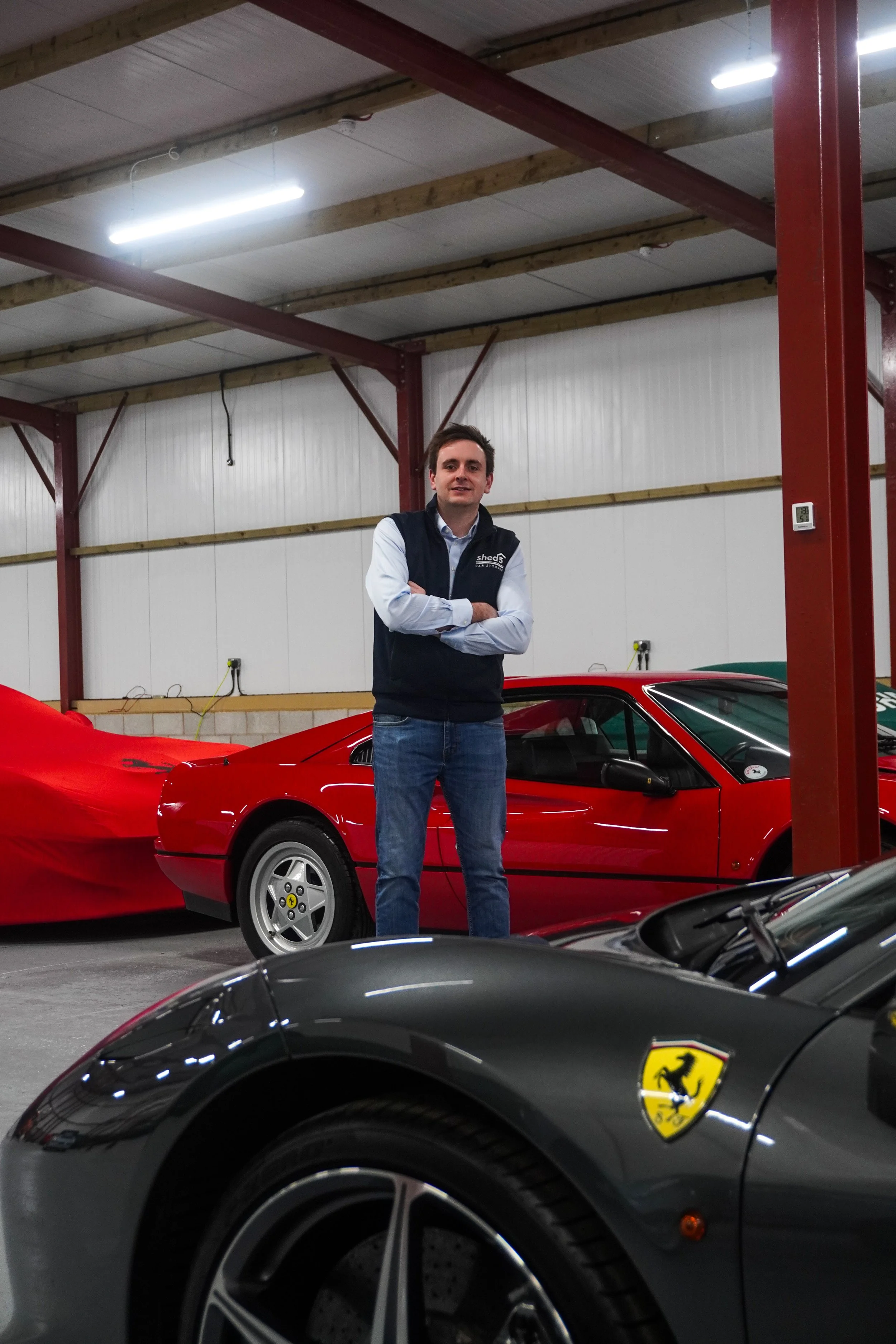 a person is standing in front of a car inside a building there  is a car in the foreground with a Ferrari badge on it. 