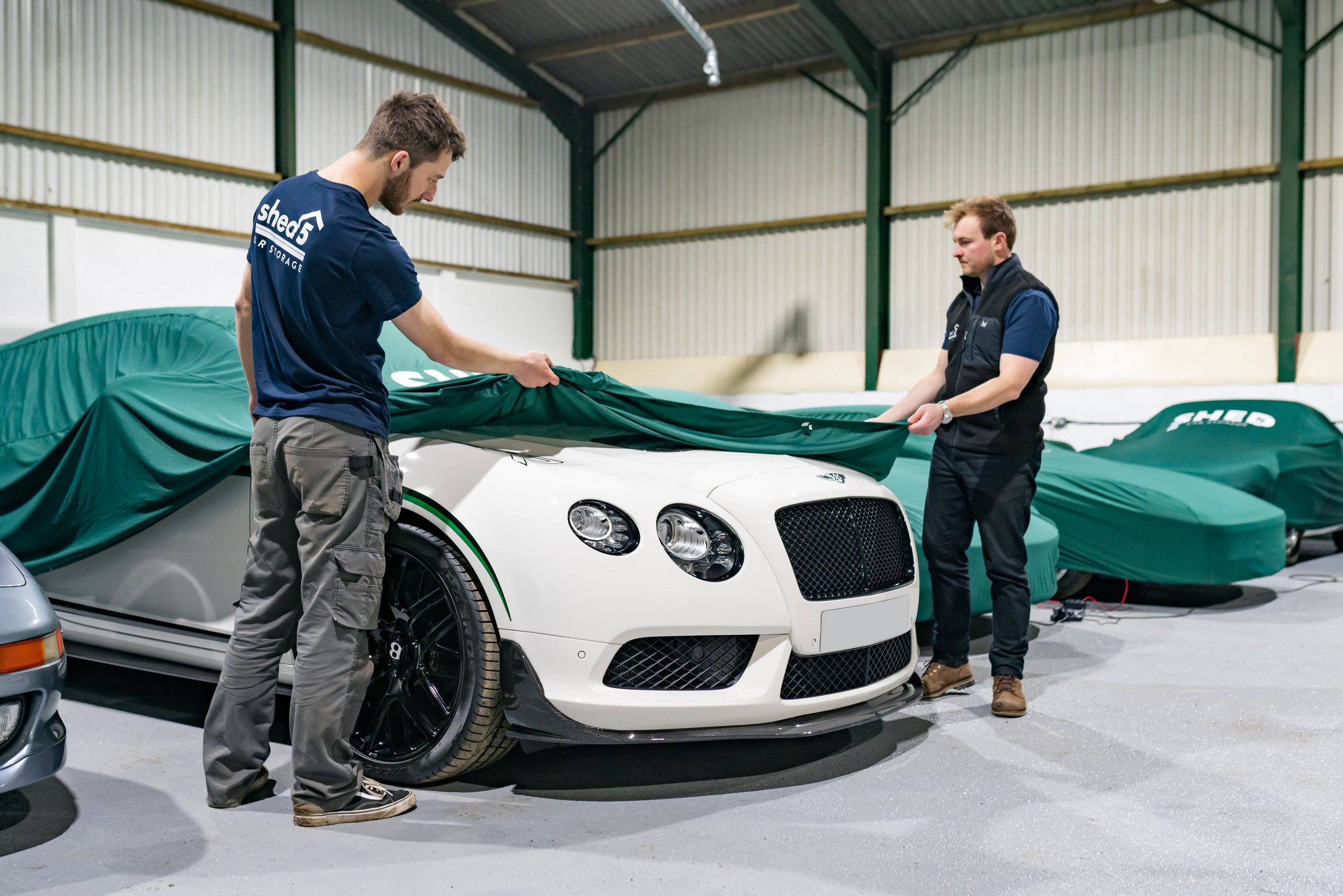 two people covering a white Bentley with a green car cover