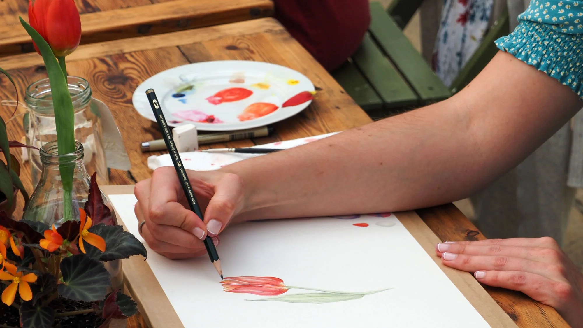 Botanical art workshops in England featuring a participant painting a tulip with watercolours at a wooden table.