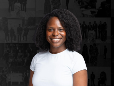 A young woman with natural curly hair smiling in front of a collage of black-and-white photos.