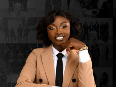 A confident woman with dark skin, styled hair, and makeup, wearing a beige blazer, white shirt, and black tie, posed in front of a collage of black and white photos.