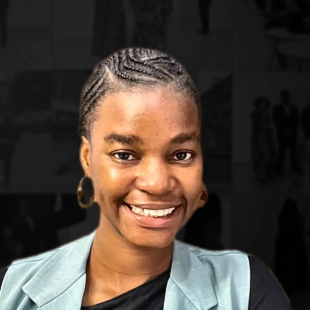A young woman with braided hair, hoop earrings, and a light gray blazer smiling in front of a dark background.