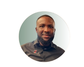 Portrait of a man with a beard and short hair, wearing a dark button-up shirt, against a neutral background.