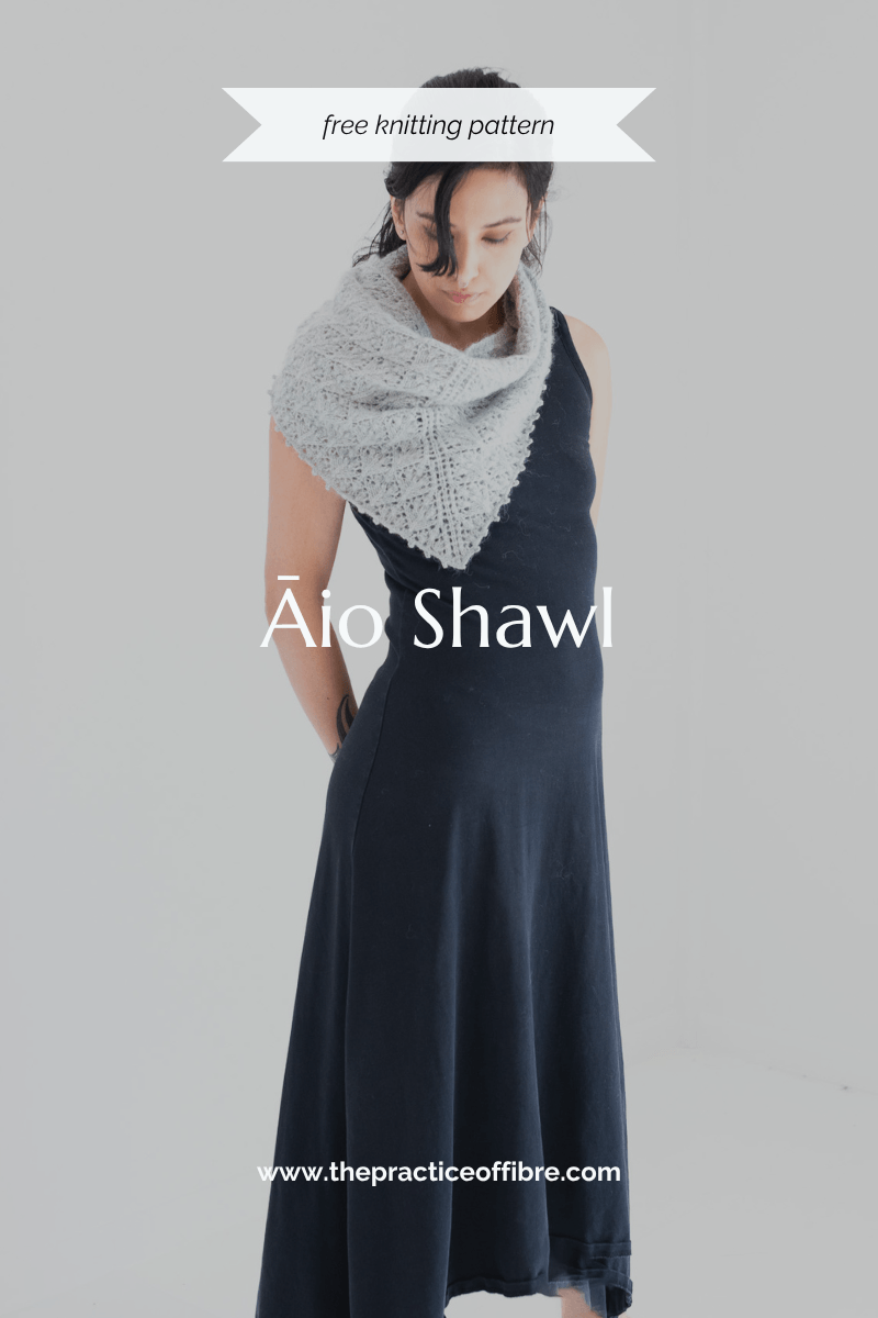 A woman in a long black dress is looking down at the floor. Wrapped around her neck loosely is a green shawl with leaf-like lace patterns.