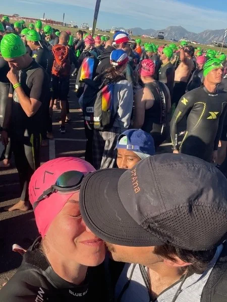 Athlete in a pink swim cap sharing a kiss with her fiance moments before the start of the Ironman 70.3 Boulder swim, surrounded by hundreds of competitors.