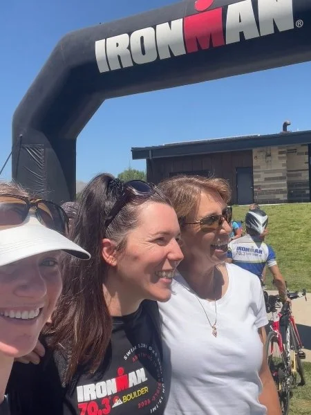 Three smiling women pose together at Ironman 70.3 Boulder the day before the race near the event venue.