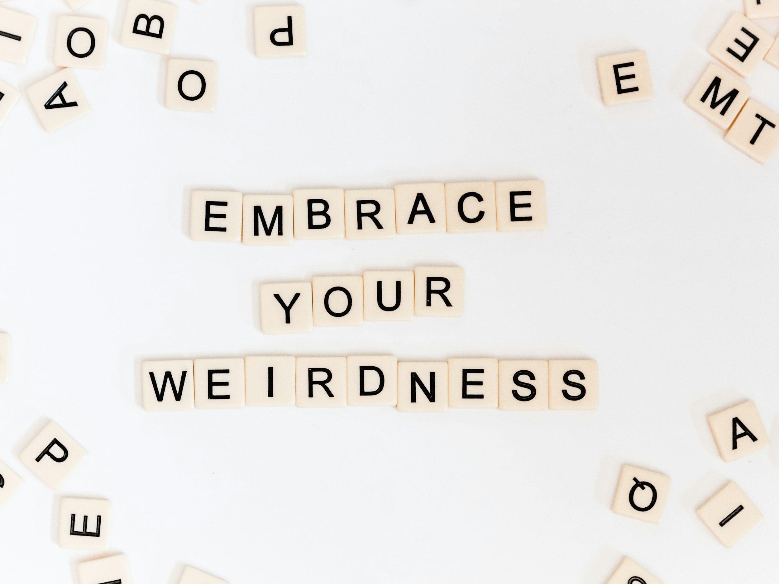 White scrabble tiles reading "Embrace Your Weirdness"