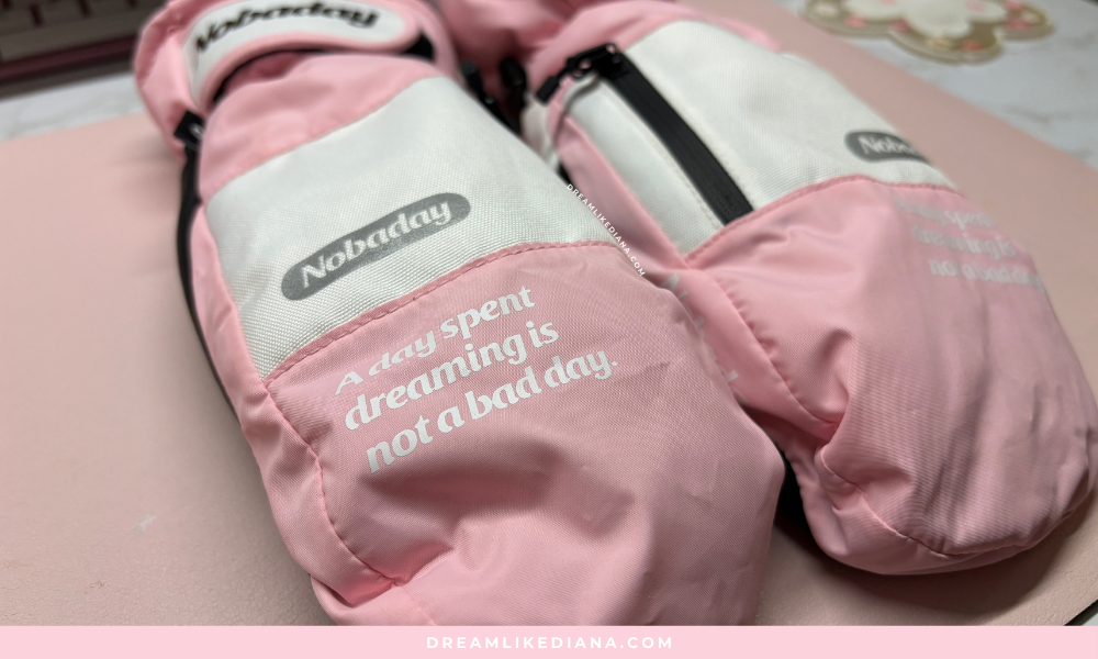 Close-up of pink and white mittens on a pink surface, displaying text: "A day spent dreaming is not a bad day." The tone is cozy and inspiring.
