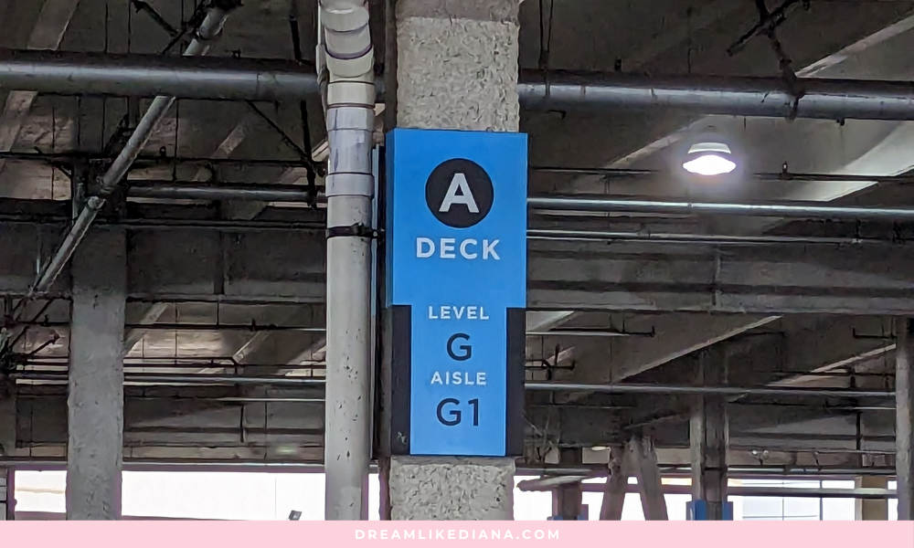 Blue parking signage on a concrete pillar in a dimly lit parking garage. It reads "A DECK, Level G, Aisle G1." Exposed pipes visible overhead.