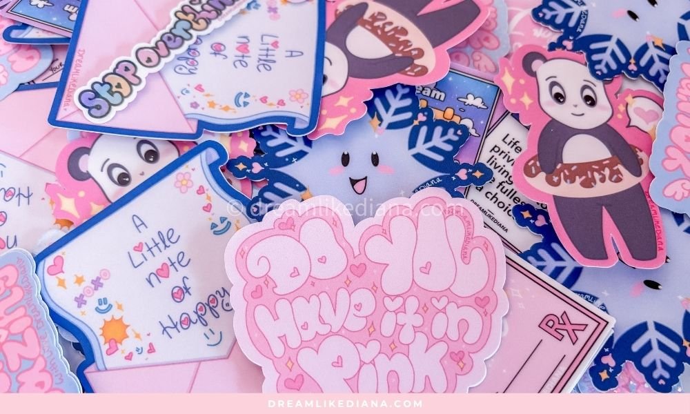 A pile of DREAMLIKEDIANA stickers in pink and blue including the "Do You Have It In Pink? heart sticker, a cute cloud character, a panda, and handwritten-style note designs
