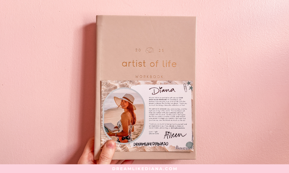 A 2025 'Artist of Life' workbook on a pink background, with an attached card featuring a woman in a hat smiling at the beach. The tone is positive and inspiring.